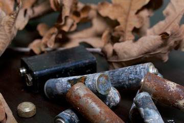Spent batteries, coated with corrosion. Different shapes and sizes. They lie on a dark background among the dead autumn leaves. Environmental protection, recycling.