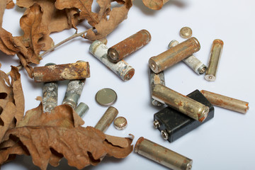 Spent batteries, coated with corrosion. Different shapes and sizes. They lie on a white background among the dead autumn leaves. Environmental protection, recycling.