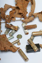 Spent batteries, coated with corrosion. Different shapes and sizes. They lie on a white background among the dead autumn leaves. Environmental protection, recycling.
