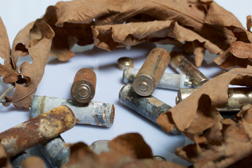 Spent batteries, coated with corrosion. Different shapes and sizes. They lie on a white background among the dead autumn leaves. Environmental protection, recycling.