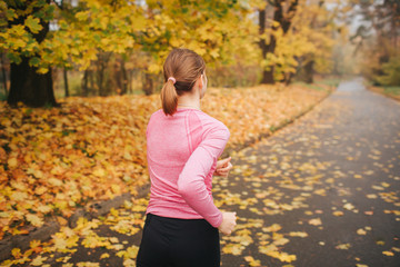 Young woman jogging alone in park. It is autumn outside. She runs on road.