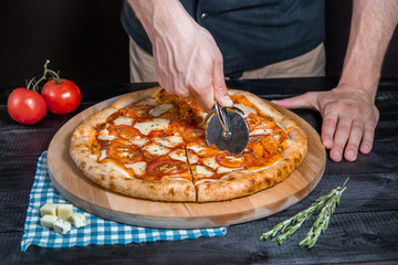 Cutting spicy pizza with salami, meat, ham, sausage, peppers, mushrooms, tomato, cheese with a...