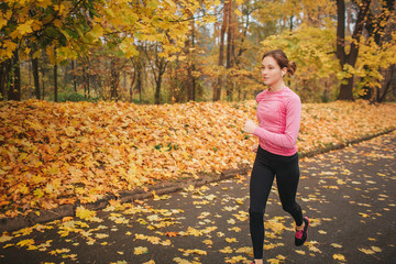 Female jogger runs on road in park. She is alone. Model training. It is autumn outside.