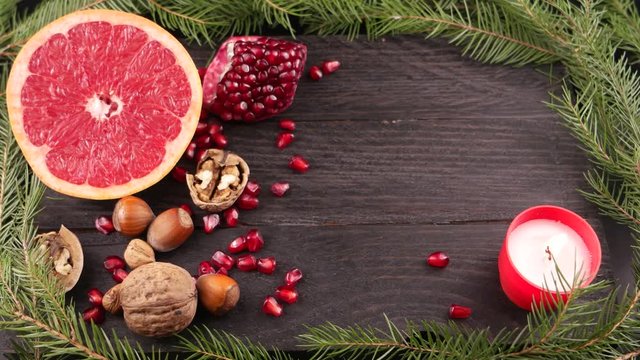Still life with a burning candle, half grapefruit, pine branch, pomegranate and nuts on the brown wooden board