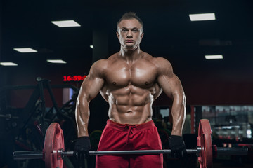 Muscular athletic bodybuilder fitness model posing after exercises in gym
