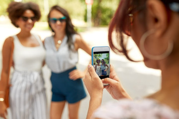 female friendship, technology and people - woman with smartphone photographing her friends in summer park