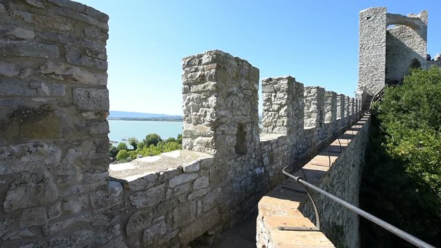 Castiglione del Lago medieval fortress fort wall in Umbria, Italy, Rocca with Medievale o Rocca del Leone tower, turquoise lake in sunny summer day