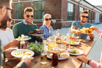 leisure and people concept - happy friends eating and drinking at barbecue party on rooftop in...