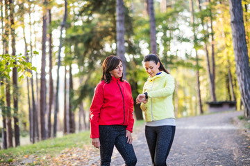 Female runners with smartwatch outdoors in forest in nature, checking the time.