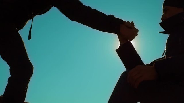 teamwork tourists business travel trip lends a helping hand. two men with backpacks hiking help each other silhouette in mountains with sunlight. slow motion video. teamwork friendship hiking help