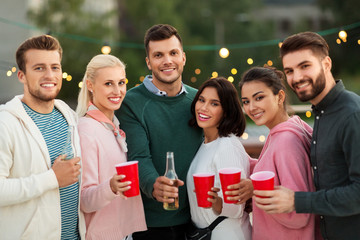 leisure, celebration and people concept - happy friends with drinks in party cups toasting at rooftop