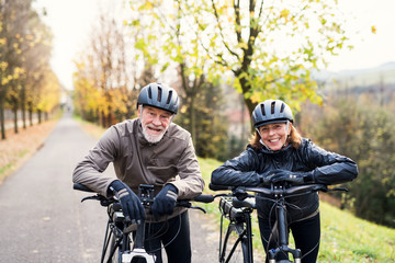 Active senior couple with electrobikes standing outdoors on a road in nature.