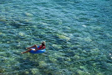 Beautiful young woman with inflatable ring relaxing in the sea.
