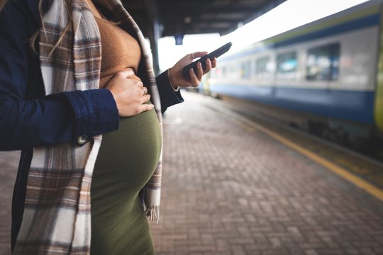 Midsection of pregnant woman using mobile phone at railway station