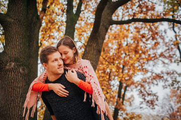 Cheerful and positive young woman sit on guy's back and leans to him. He holds her and look to...