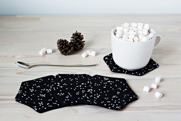 Black fabric coasters,  white cup with marshmallows and spoon on the table