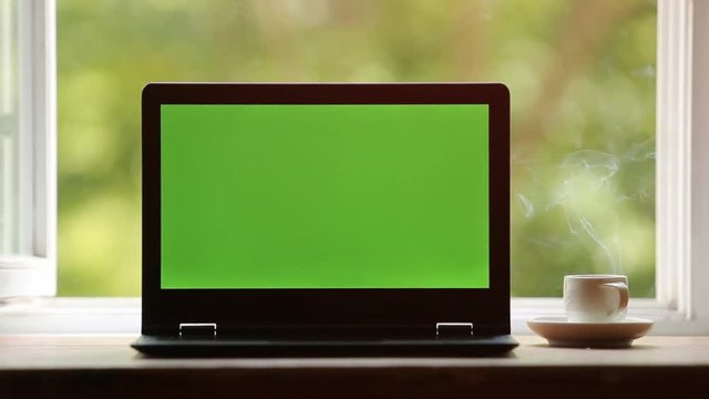 Laptop with track green screen on a desktop there is a hot steaming cup of coffee