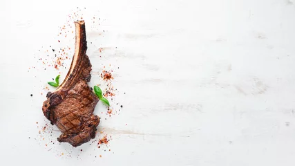 Schilderijen op glas Biefstuk op het bot. tomahawk steak op een witte houten achtergrond. Bovenaanzicht. Gratis exemplaar ruimte. © Yaruniv-Studio