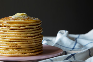 Stack of homemade pancakes with butter on pink plate, side view. Closeup. Copy space.