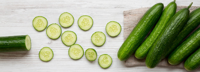 Fresh raw organic green cucumbers over white wooden background, overhead view. Flat lay, from above, top view.