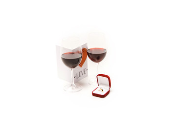 Two glasses with red wine, lovely postcard with heart and ring box isolated on white