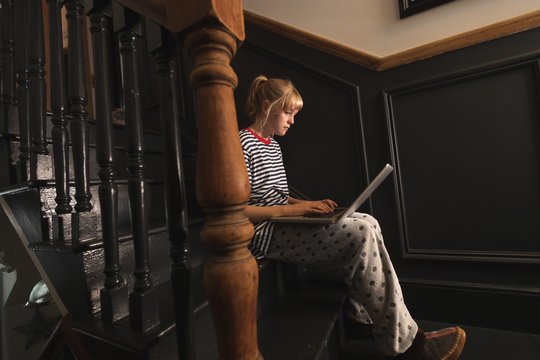 Woman using laptop on stairs at home