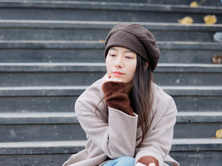 Portrait of pensive young woman looking away thinking sitting on wooden steps in a park outdoors background late autumn, she put her head on her hands.