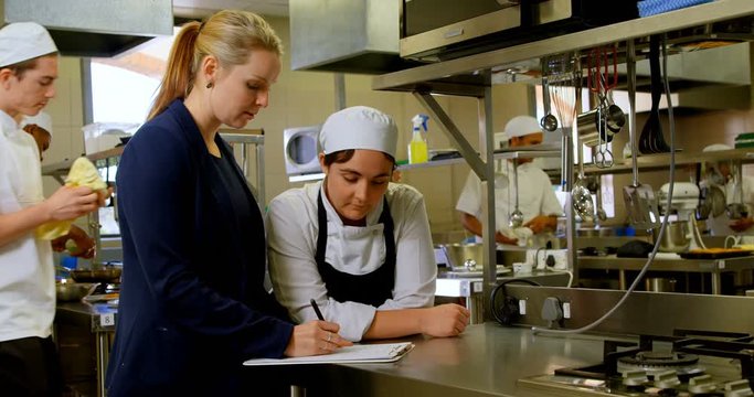 Female manager and female chefs discussing over clipboard 4k