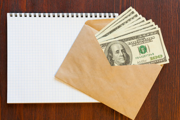 Several hundred dollar banknotes in an envelope and a notebook  on a wooden surface. Copy space.