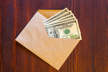 Several hundred dollar banknotes in an envelope on a wooden surface