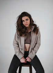 Girl with chic hair, sits on a chair in a studio, on a grey background