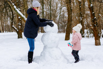 Fototapeta na wymiar mom and daughter make a snowman out of snow