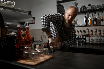Brutal young barista in an apron makes coffee at the bar in a modern cafe