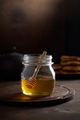 A jar of raw golden honey with a wooden honey dipper