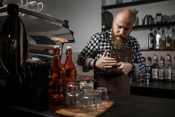 Brutal young barista in an apron makes coffee at the bar in a modern cafe
