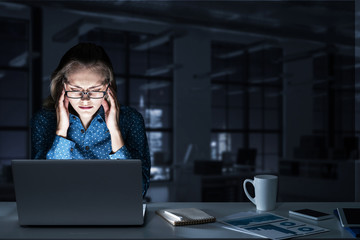 Attractive blonde working on laptop in dark office. Mixed media