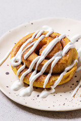 Homemade pumpkin cinnamon bun roll sweet autumn baked dessert with cream cheese sauce in spotted ceramic plate over white marble table. Close up.