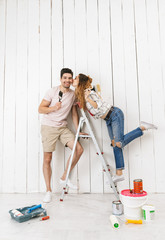 Full length photo of beautiful couple man and woman standing on ladder, while painting white wall...