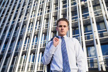 Businessman in classy suit holding his jacket on background of modern office skyscraper.