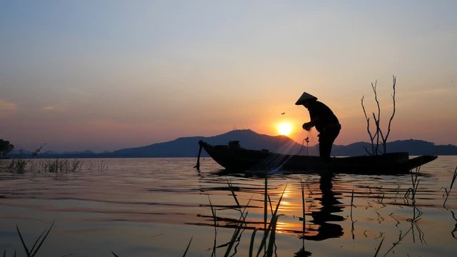 Silhouette scene of Fisherman on boat fishing with a fishnet. He use old traditional fishing equipment for fishing in The lake. Bang Phra Lake - Eastern of Thailand