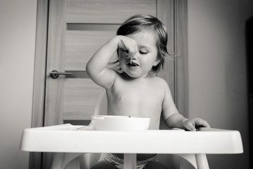 Child little baby girl eating in high chair, black and white, lifestyle, motion