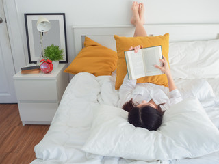 asian woman reading book on bed in the morning