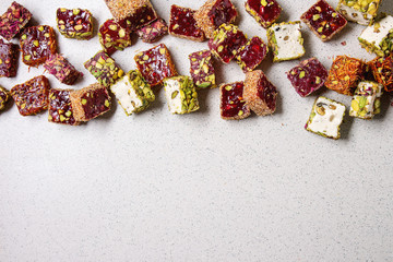Obraz na płótnie Canvas Variety of traditional turkish dessert Turkish Delight different taste and colors with rose petals and pistachio nuts over grey spotted background. Flat lay, copy copy space