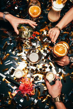 cropped image of friends with luxury watches celebrating alcohol at table covered by golden confetti