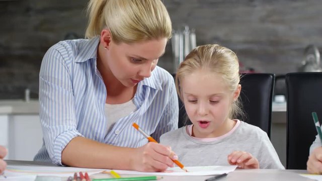 Beautiful Caucasian woman and cute little daughter drawing together with colored pencils at kitchen table in home
