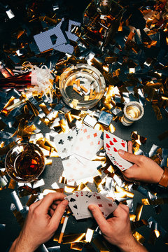 cropped image of male friends and playing poker with alcohol and cigarettes at table covered by golden confetti