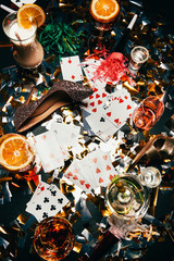 top view of female shoes on high heels, playing cards, alcoholic cocktails and party horns on table covered by golden confetti
