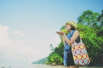 asian woman blowing dandelion flower standing on the beach