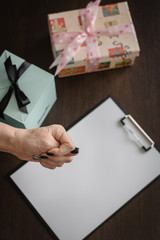 Gifts for the holidays will not be a negative reaction, not a desire to give gifts. Female hand shows negative against the background of gifts and empty wish list.