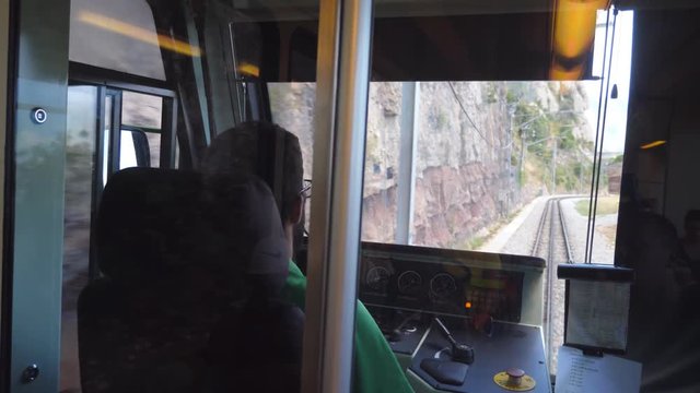 Unrecognizable train driver drives electrical train among mountain road. Point of view from driver cabin to railway tracks. Rear back view POV Slow motion Close up